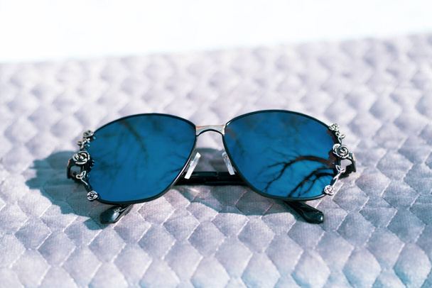 Модна модель сонцезахисних окулярів з великими блакитними лінзами для жінок зі спеціальною дизайнерською стрічкою на вулиці в сонячний день. Вибірковий фокус
  - Фото, зображення
