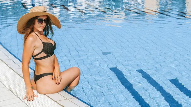 Summer sale. Young sexy woman in Sun hat, bikini swimsuit, sunglasses relaxing in blue pool water. Summer luxury vacation in spa resort pool - Photo, image
