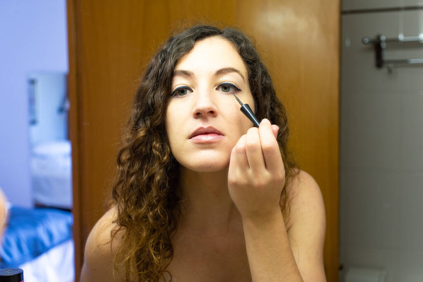 Young woman putting on makeup in front of a mirror. Close-up using eye-liner, drawing the eye line. - Zdjęcie, obraz