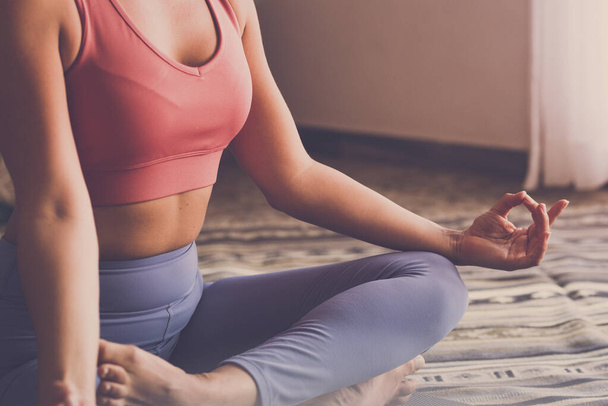 Close up of healthy body and soul. Cropped view of sportive American woman meditates on yoga mat, making mudra gesture, sitting in lotus after sport exercise training at home - Photo, Image