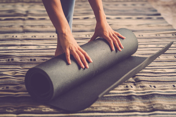 Κοντινό πλάνο των γυναικών χέρια απογειώνεται στρώμα γιόγκα από το πάτωμα μετά την άσκηση εσωτερική προπόνηση ενεργό καθημερινή συνεδρία των ασκήσεων - Φωτογραφία, εικόνα