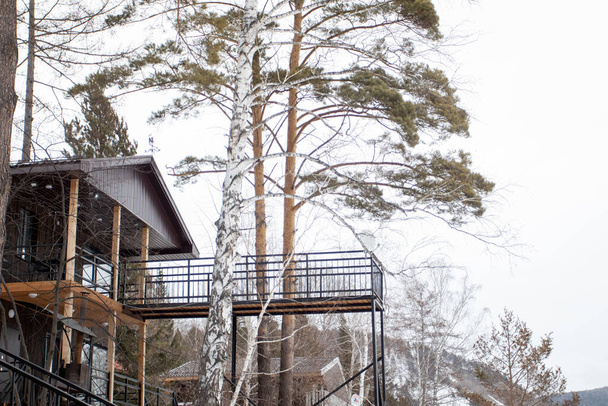 Modern kétszintes faház magas terasszal és kilátó fedélzettel az erdőben magas fenyők között. - Fotó, kép