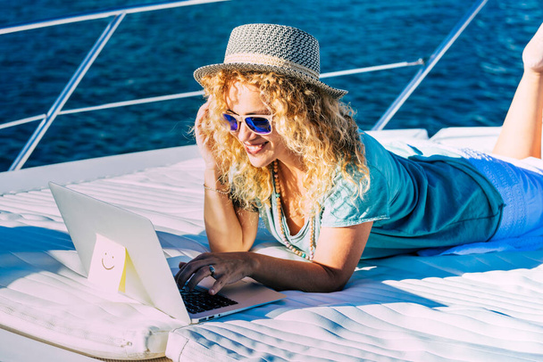 Mulher alegre trabalhar ao ar livre com computador portátil deitar em um barco desfrutando de liberdade e conexão à internet - Foto, Imagem