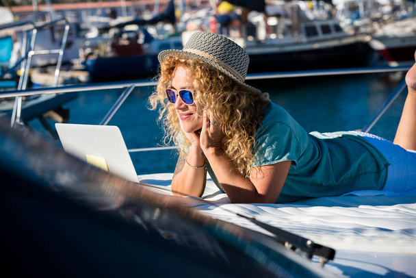 女性の笑顔は夏休みにボートのデッキに横たわり、ラップトップを見る - 写真・画像