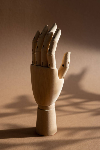 Рука дерев'яної ляльки змушує пальці торкатися, направляти, переміщатися на коричневому тлі в студії з темними тінями вид збоку вертикальний
 - Фото, зображення