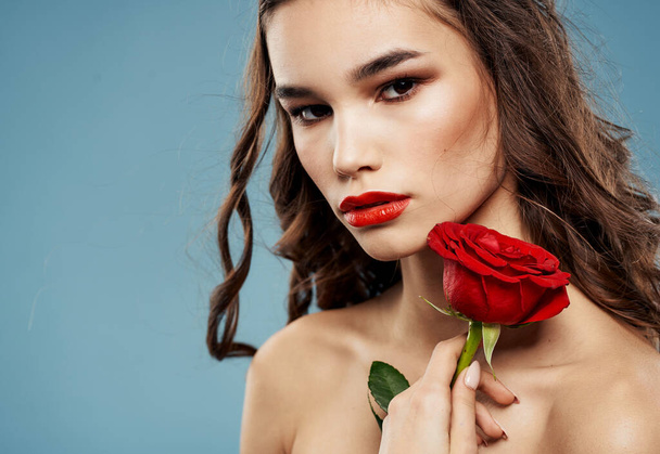 Jolie brune avec une rose rouge près du visage sur un fond bleu - Photo, image