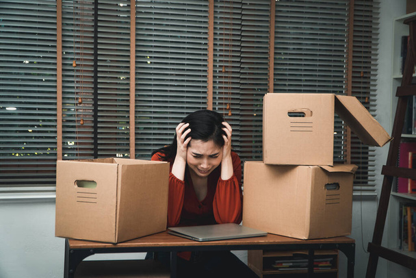 Smutna Azjatka Pakuje rzeczy w kartonowe pudełko i płacze na biurku w biurze Po zwolnieniu i bezrobociu. Koncepcja wpływu na pogorszenie koniunktury gospodarczej i zarządzanie porażką - Zdjęcie, obraz