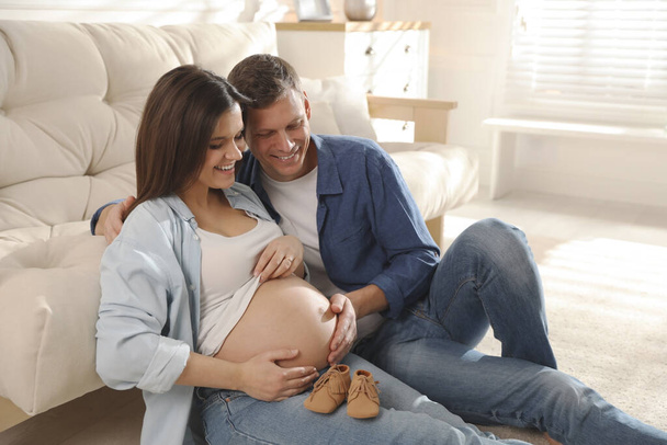 Young pregnant woman and her husband with baby's shoes at home - Foto, imagen