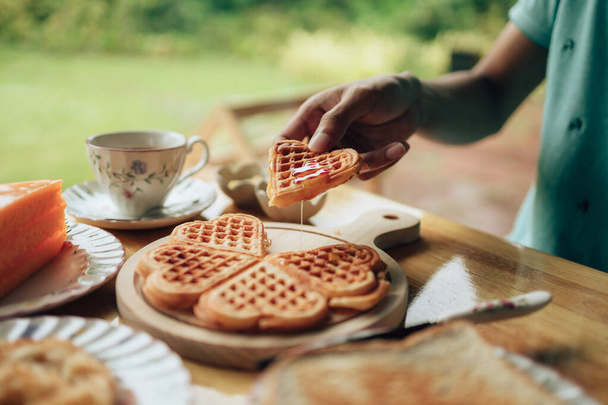 Hand pick  piece fresh waffles on wood plate. Waffle and dessert concept. - Фото, изображение