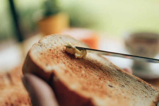 Knife spreading butter on toast bread in hands in the morning breakfast. Coffee and dessert concept. - Fotoğraf, Görsel