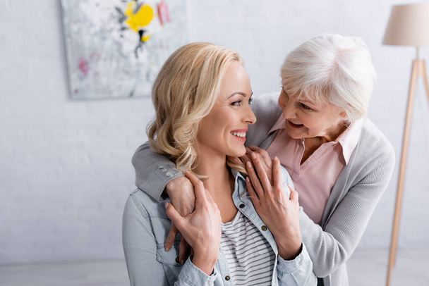 Smiling woman touching hands of grey haired mother at home  - Foto, afbeelding