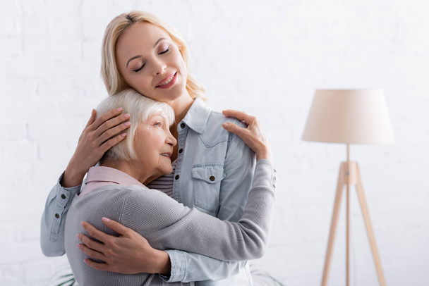 Woman and daughter with closed eyes hugging in living room  - Фото, зображення