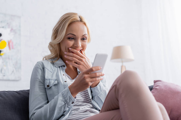 Amazed woman using cellphone on couch  - Photo, Image