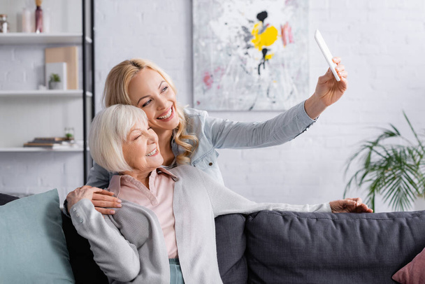 Smiling woman taking selfie with senior parent at home - Foto, Imagen