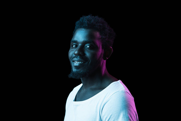 Молодой счастливый афроамериканец, изолированный на тёмном фоне в неоновом свете - Фото, изображение