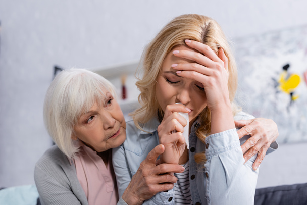 Elderly woman hugging crying daughter with napkin at home  - Photo, Image