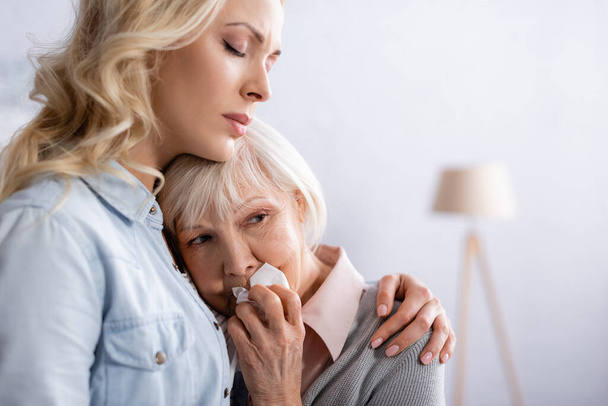 Mujer calmando a la madre mayor con servilleta en casa  - Foto, Imagen