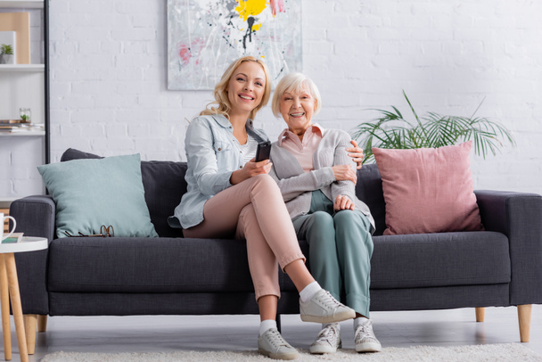 Smiling woman sitting near daughter with remote controller  - Photo, Image