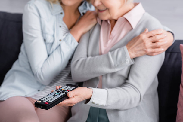 Cropped view of senior woman holding remote controller near daughter on blurred background  - Foto, Imagen
