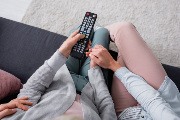 Top view of woman holding hand of senior mother with remote controller on couch  - Valokuva, kuva