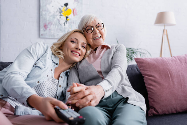 Cheerful senior woman sitting near adult daughter with remote controller on blurred foreground  - Valokuva, kuva
