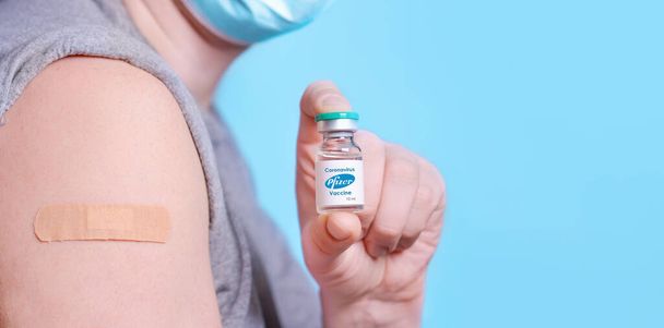 Charkov. Ukrajina. 24. prosince 2020.Pacient v lékařské masce a náplasti na rameni má lahvičku koronavirové vakcíny s logem Pfizer.Zdravotní péče, koncepce očkování. Kopírovat prostor. - Fotografie, Obrázek