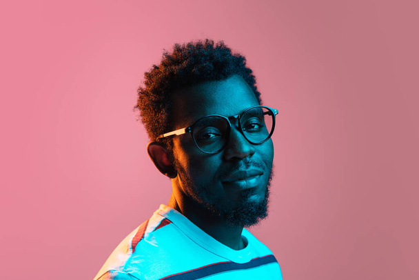 Young serious African-American man isolated on pink background in neon light - Фото, изображение
