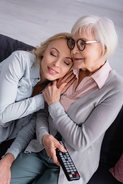 Woman sitting near senior mother with remote controller  - Foto, Imagen