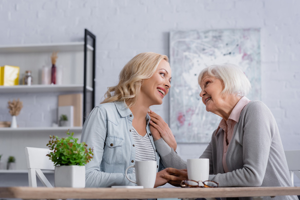 Cheerful women talking near cups and eyeglasses in living room  - Photo, Image