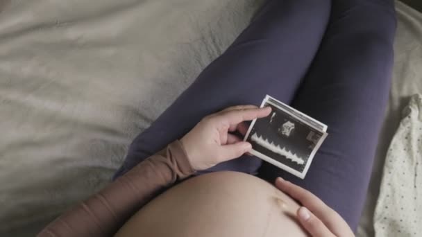 ожидая беременную женщину с большим животом, смотрящую на УЗИ дома - Кадры, видео