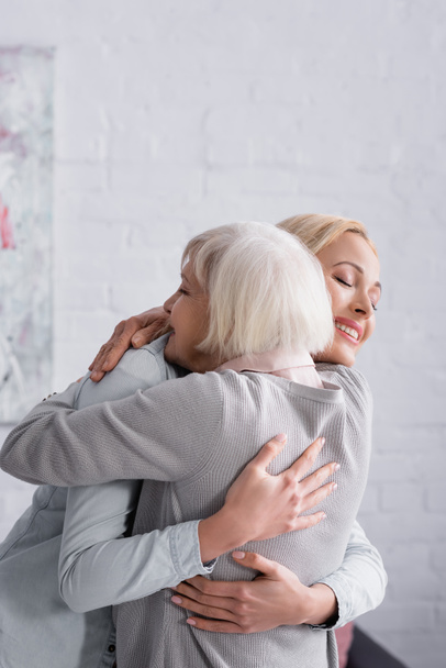 Donna allegra che abbraccia il genitore dai capelli grigi in soggiorno  - Foto, immagini