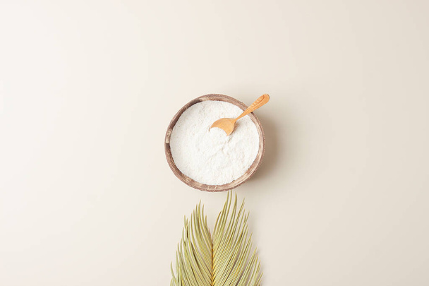 Colágeno en polvo en tazón con cuchara de medir con hojas de palma sobre fondo beige pastel. Colocación plana, espacio de copia - Foto, Imagen