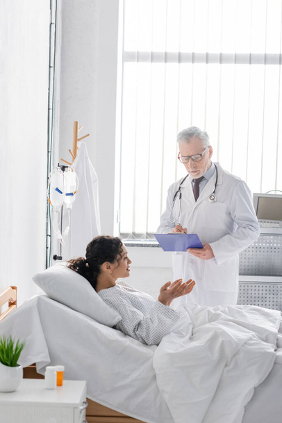 african american woman gesturing while talking to doctor writing diagnosis on clipboard - Photo, image