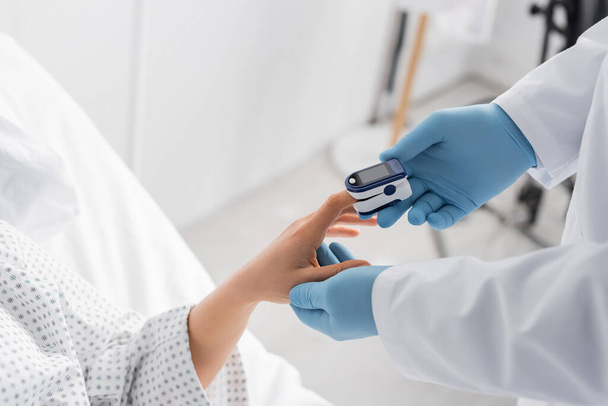 vista ritagliata del medico in guanti di lattice utilizzando pulsossimetro sul dito del paziente - Foto, immagini