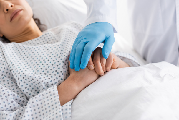 partial view of doctor in latex glove touching hands of diseased african american woman in hospital - Фото, изображение