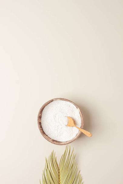 Colágeno en polvo en tazón con cuchara de medir con hojas de palma sobre fondo beige pastel. Colocación plana, espacio de copia - Foto, Imagen