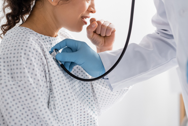 visão parcial do médico em luvas de látex examinando tosse afro-americana com estetoscópio - Foto, Imagem