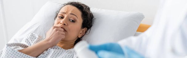 worried african american woman lying in hospital bed near doctor with medication on blurred foreground, banner - Foto, imagen