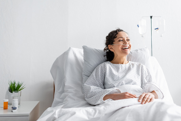 felice donna afroamericana ridere mentre seduto nel letto d'ospedale - Foto, immagini