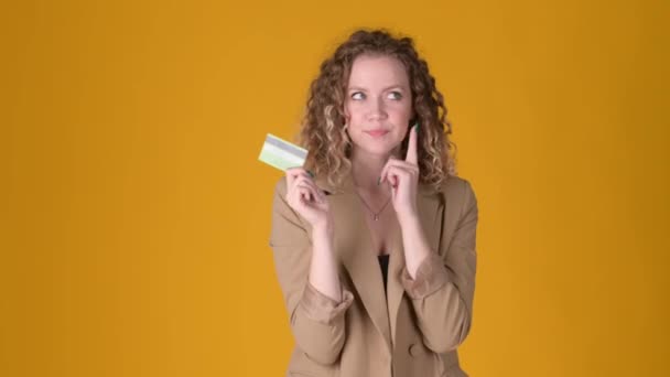Cheerful young girl with curly hair hold credit bank card having great new idea say yes isolated on yellow studio background. People lifestyle concept. - 映像、動画