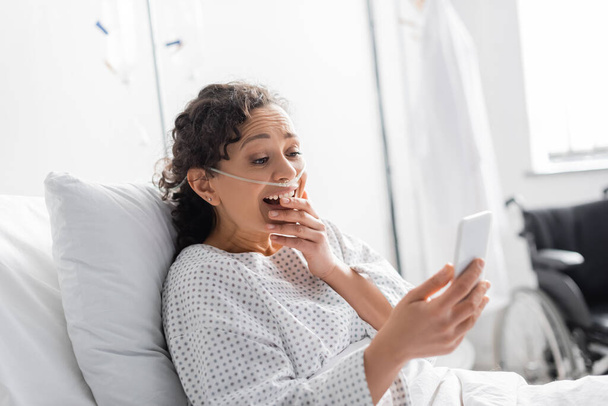 mulher afro-americana surpreendido cobrindo boca enquanto olha para o celular na clínica - Foto, Imagem