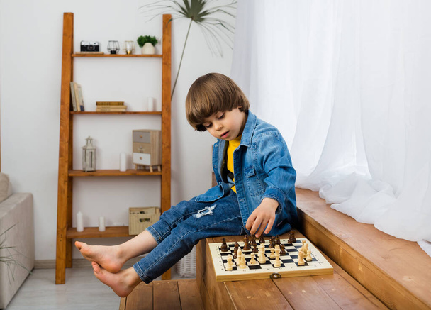 little boy is playing chess on a chessboard in a room - Fotoğraf, Görsel