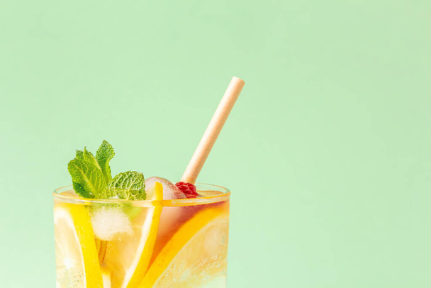 Glass of ice tea with ice, lemon and mint leaves on a green background. Summer cold drink lemonade with paper straw. Copy space - Foto, imagen