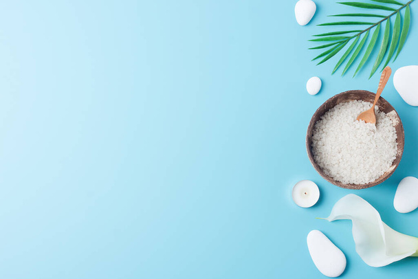 Spa achtergrond met kom van zout, witte stenen, kaarsen, palmblad en witte bloem op blauw. Vlakke lay, kopieerruimte - Foto, afbeelding