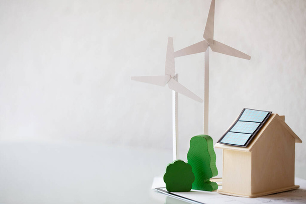 Rüzgar türbininin kağıt modeli, yeşil ağaçlar, masada güneş panelleri olan ahşap ev. Yakın çekim. - Fotoğraf, Görsel