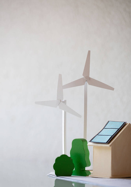 Paper model of wind turbine , green trees , wooden house with solar panels on the table. Closeup - Photo, Image