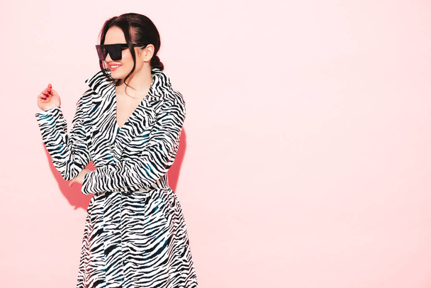 High fashion portrait of young beautiful brunette woman wearing nice trendy summer zebra coat.Sexy fashion model posing near pink wall in studio.Fashionable female in sunglasses - Фото, зображення