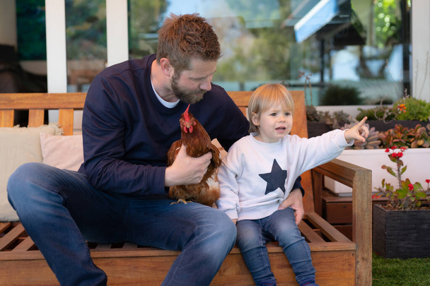 Vater und Sohn amüsieren sich gemeinsam mit einem Huhn im Garten - Foto, Bild