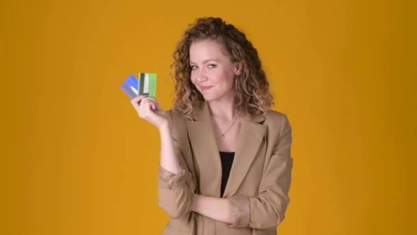 Cheerful young girl with curly hair Point hand on credit bank card showing thumb up like gesture isolated on yellow studio background. People lifestyle concept. - Imágenes, Vídeo