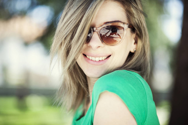 κοντινό πορτραίτο όμορφης γυναίκας που φοράει γυαλιά ηλίου και ποζάρει στο πάρκο την ημέρα - Φωτογραφία, εικόνα